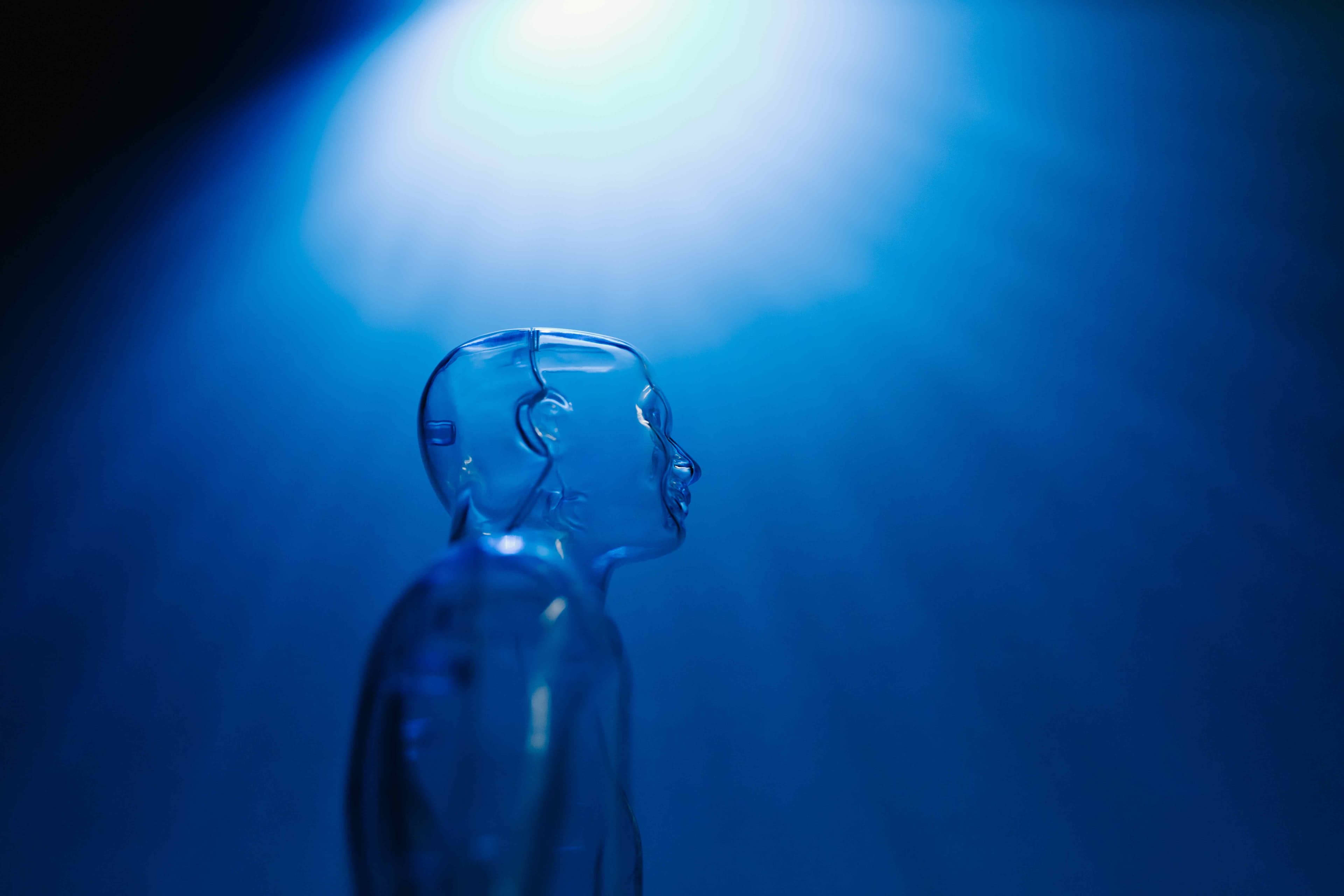 A see-through human shaped piece of plastic that is underneath a light shining down on it inside of a dimly lit blue room.