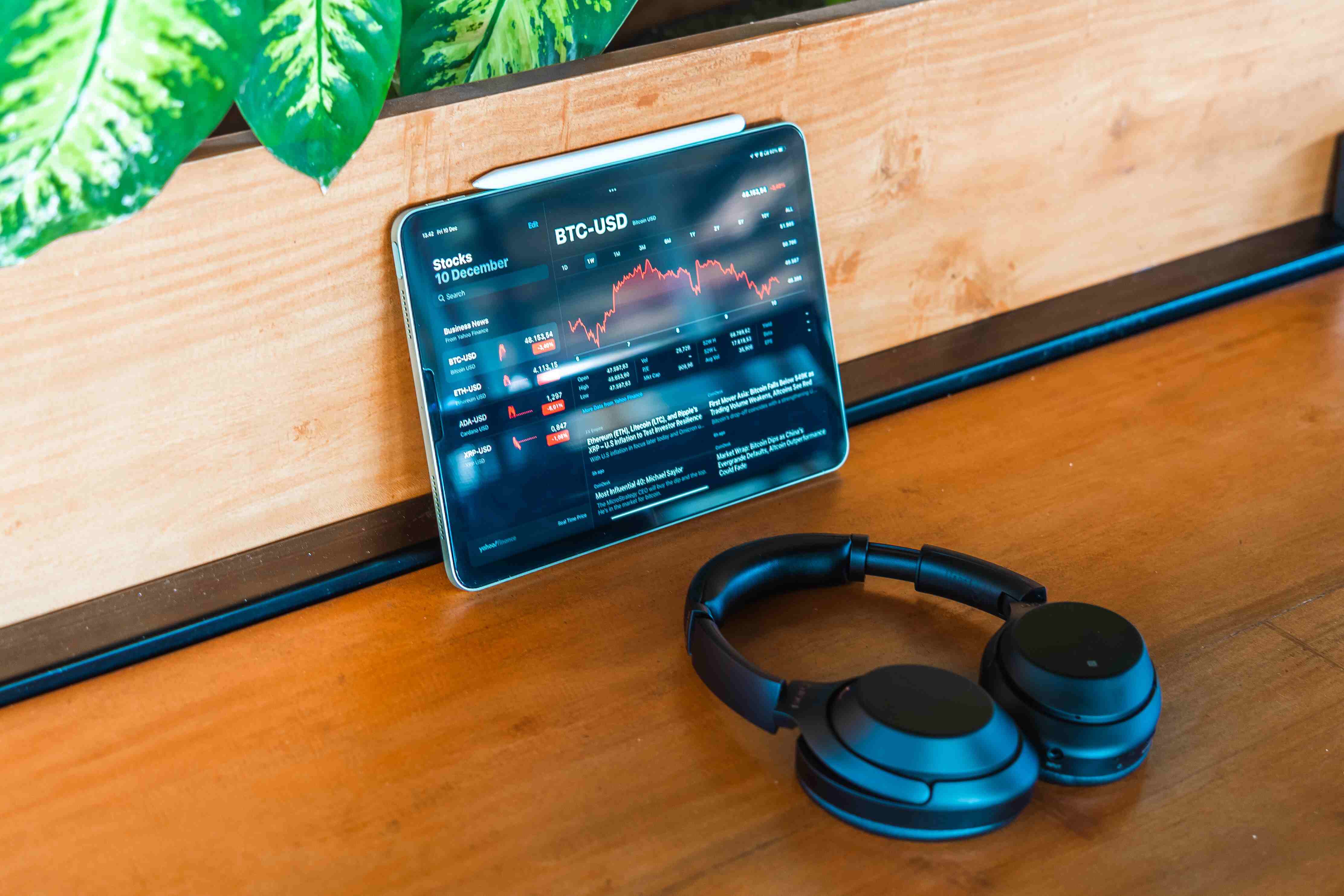 Apple iPad with an investing app open that is showing the value of Bitcoin with a red line chart sitting on a wooden table.