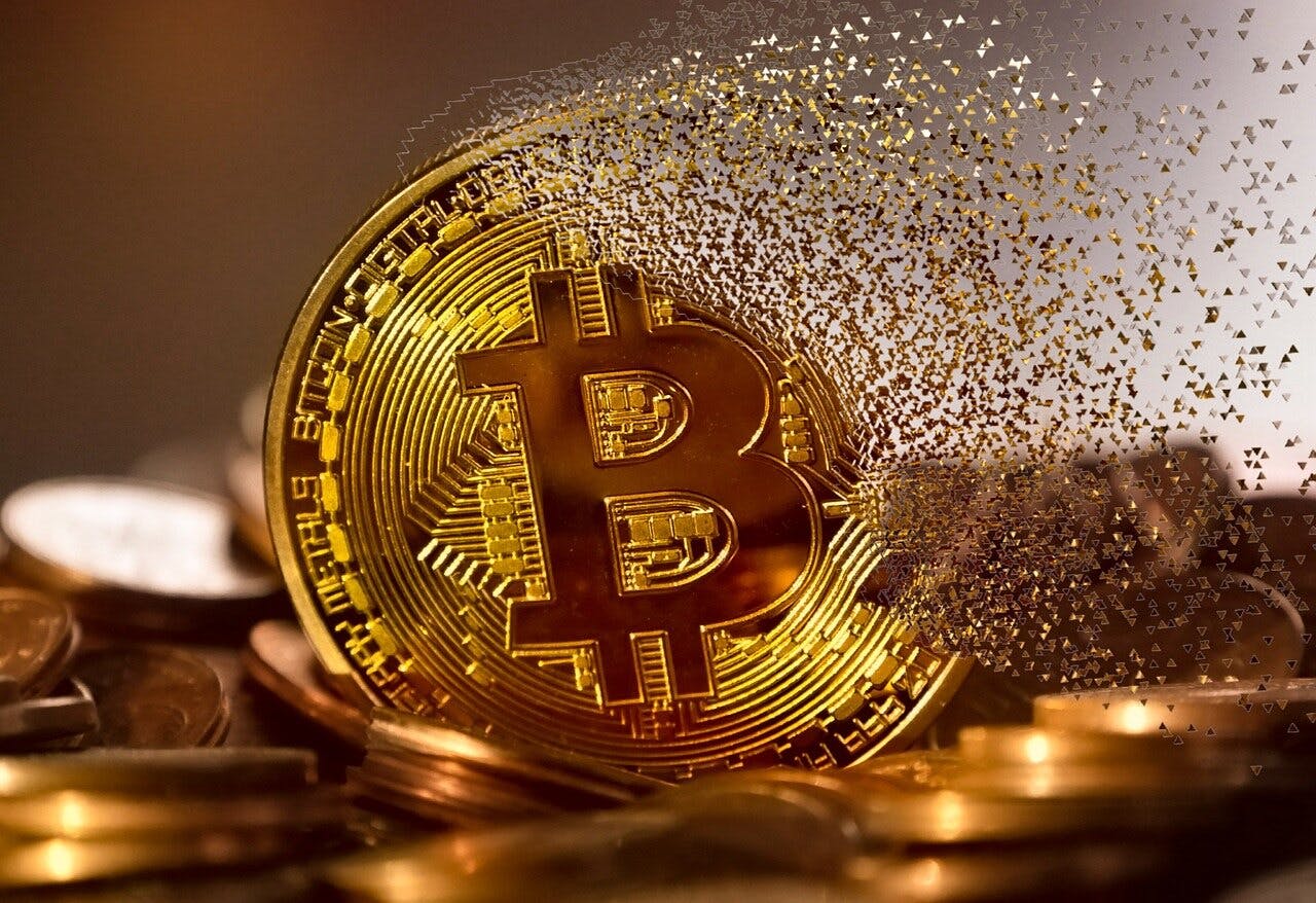 A single golden Bitcoin crypto coin with its logo on the face of the coin fading away into dust surrounded by other coins.