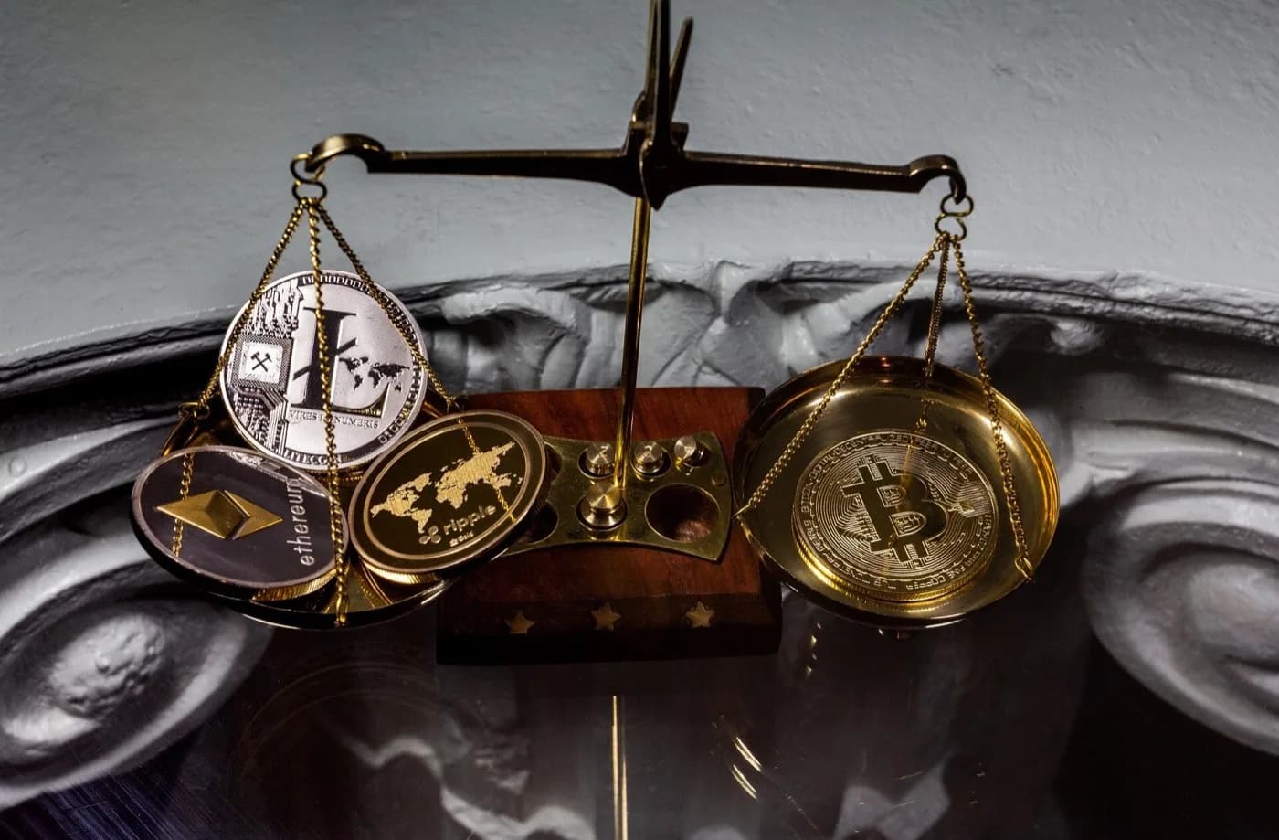 A balance containing many shiny crypto coins with Ethereum, Litecoin, and Ripple on the left with Bitcoin by itself on the right.