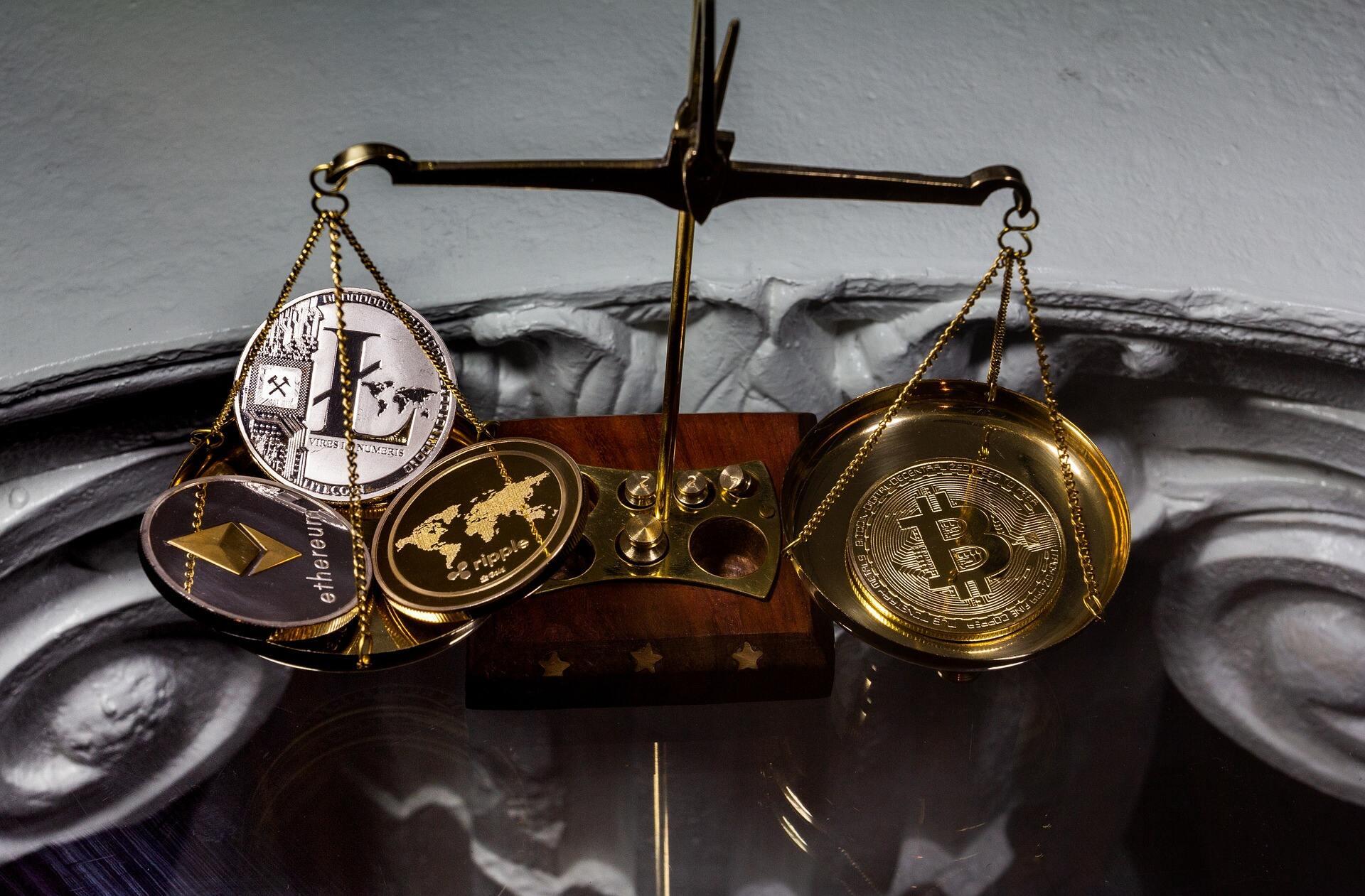 A balance containing many shiny crypto coins with Ethereum, Litecoin, and Ripple on the left with Bitcoin by itself on the right.