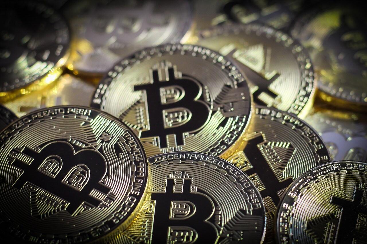 A lot of Bitcoin shiny crypto coins that are gold with the Bitcoin symbol on them in the color black all on top of each other.