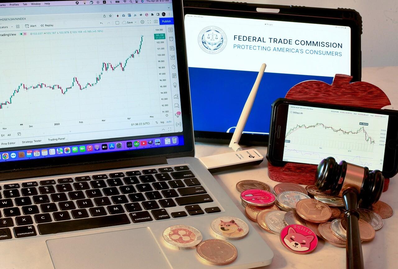 A Macbook laptop showing a cryptocurrency trading screen next time a pile of crypto coins and an iphone showing another screen.