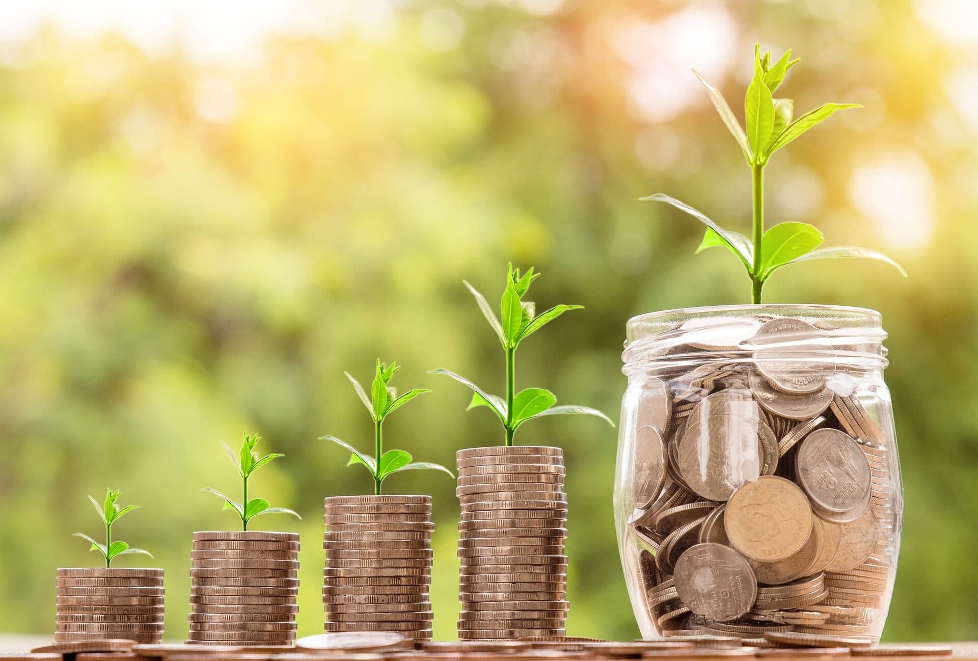 Stacks of coins increasing as they go to the right with little plants on the top of them all next to a jar filled with coins.