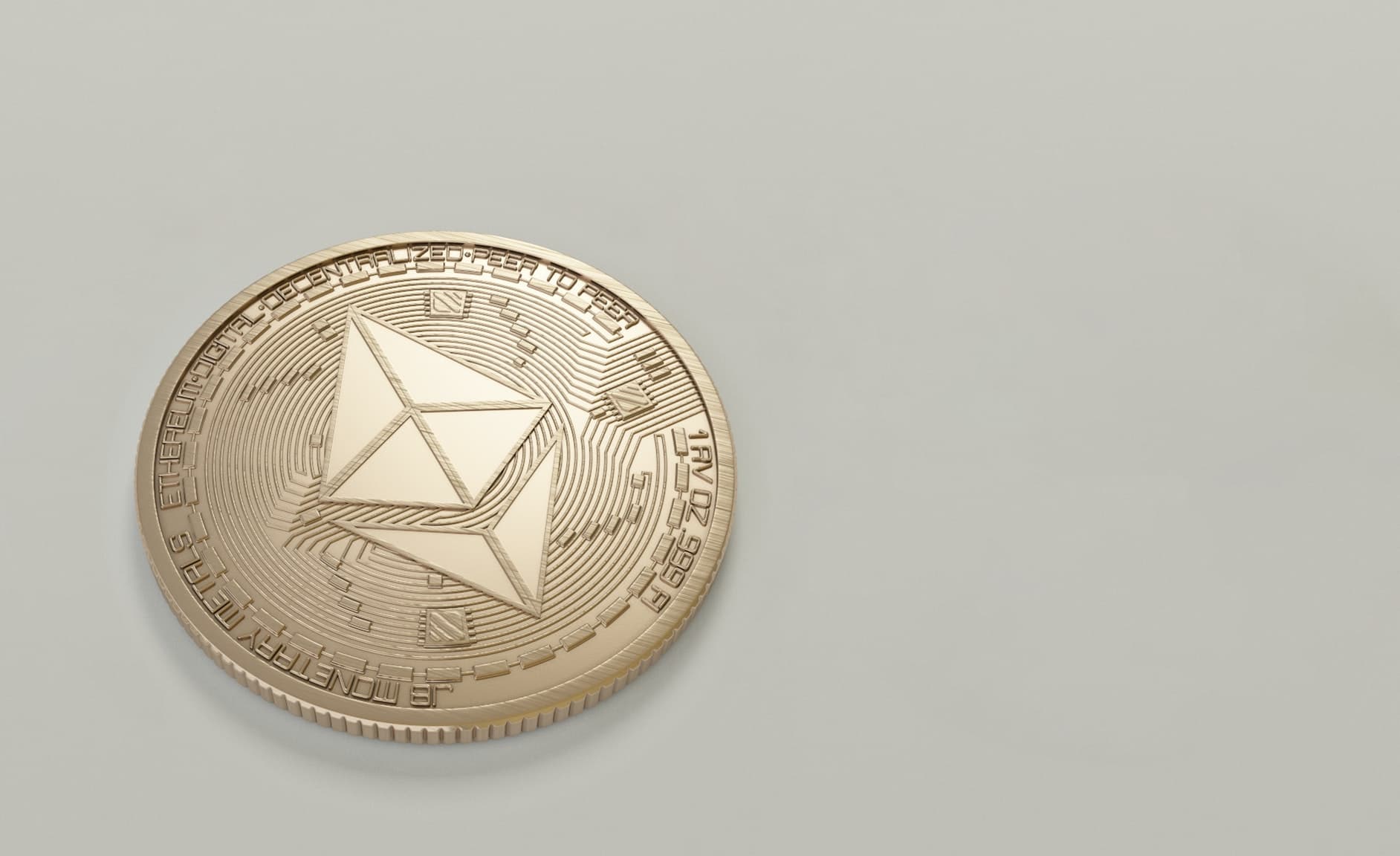 A golden Ethereum coin with fine sketches and etchings that is resting on top of a very lightly colored table or surface.