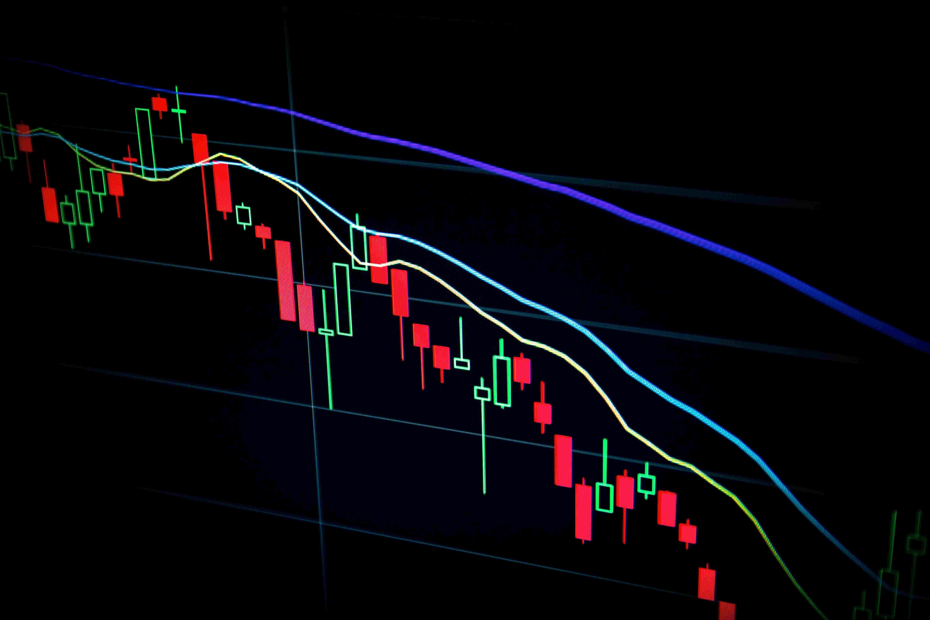 Cryptocurrency candle chart on a screen that is heading downward with three lines above it colored blue, green, and yellow.