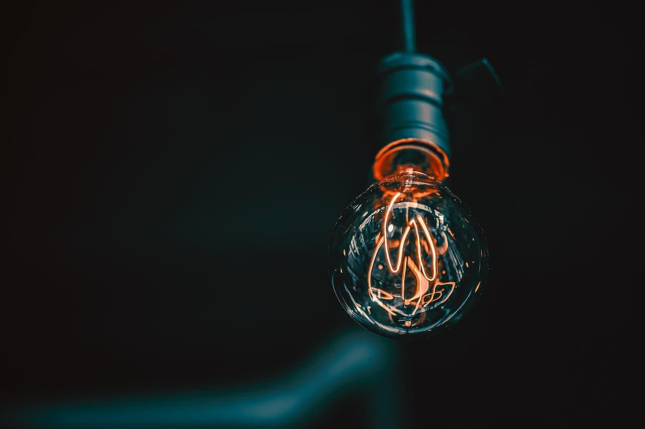 A black lightbulb wire in a block room with a shiny glass light bulb plugged into it with the coil slightly lit up orange.