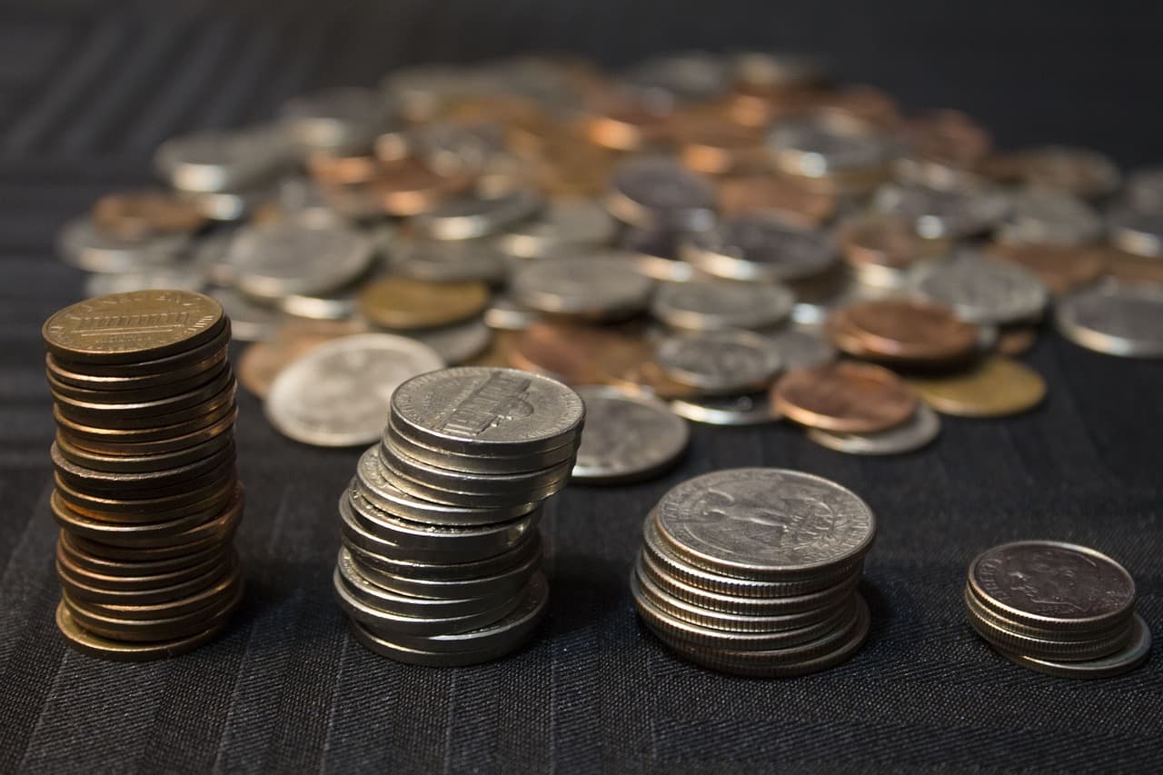 Four different stacks of coins with each one a different one of nickels, pennies, dimes, and quarters in front of more coins.