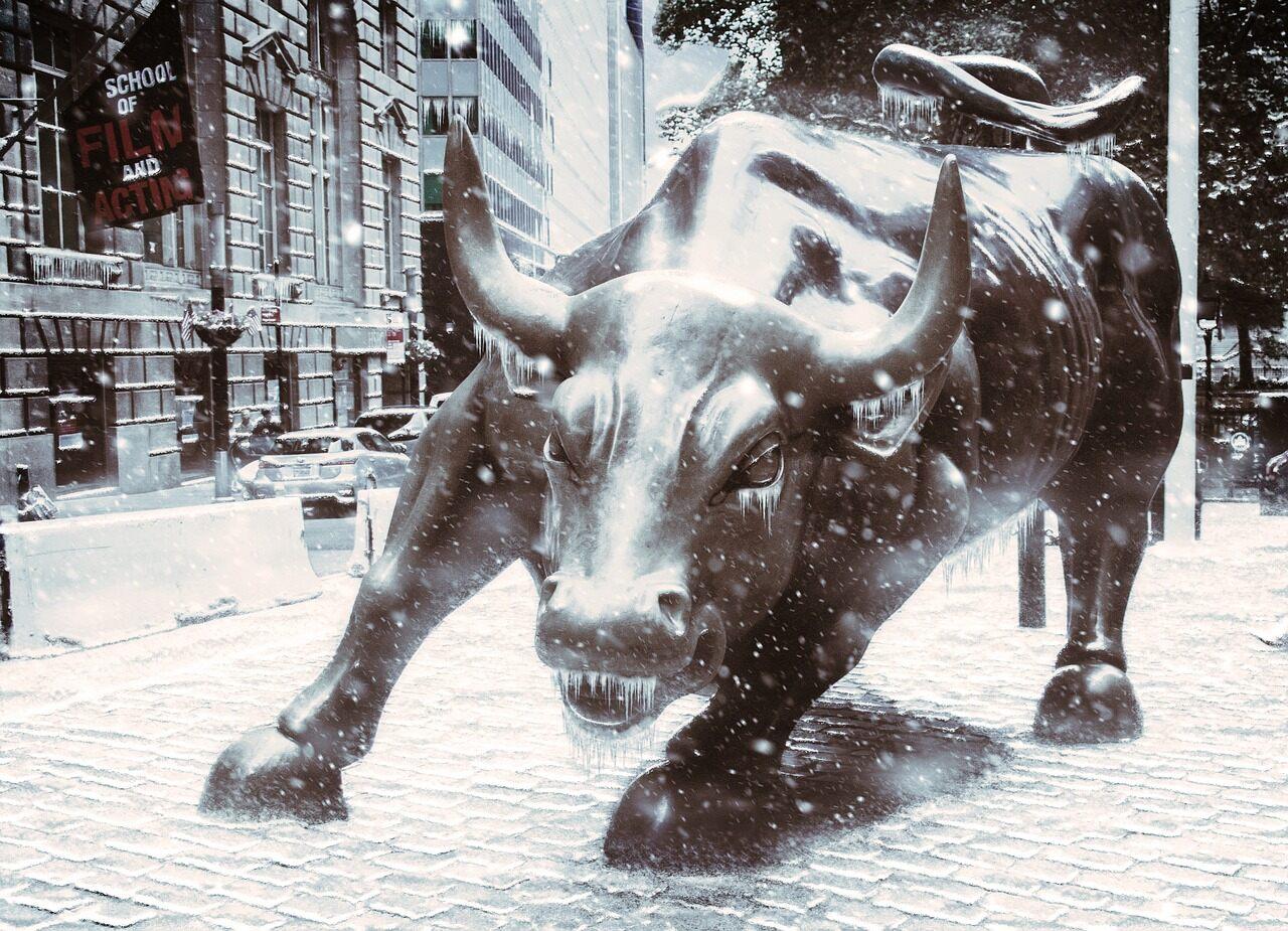 The large metal bull statue that sits in wall street in New York while it is snowing outside and the pathway has snow on it.