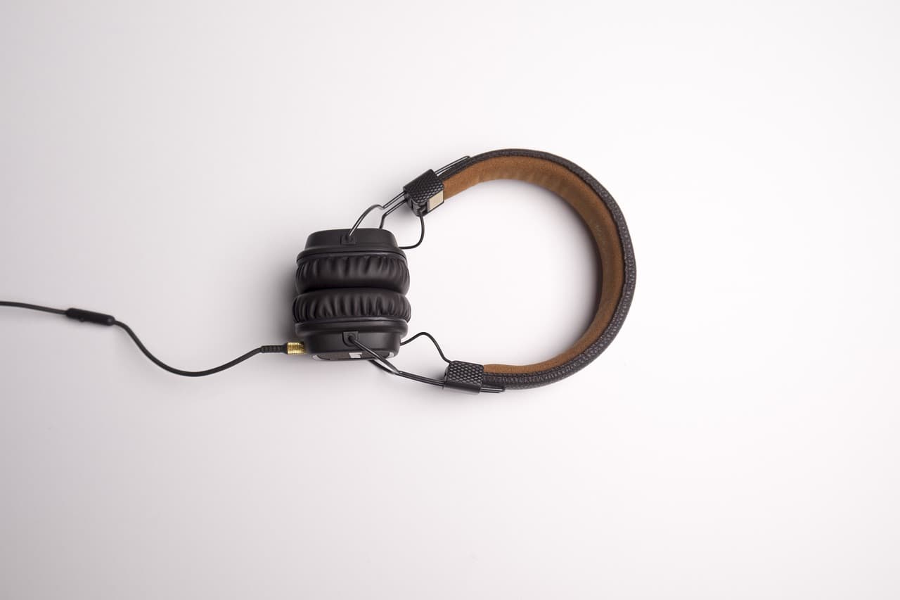 A set of black video gaming headphones on a white table with a brown leather headband on them and a black wire coming from them.