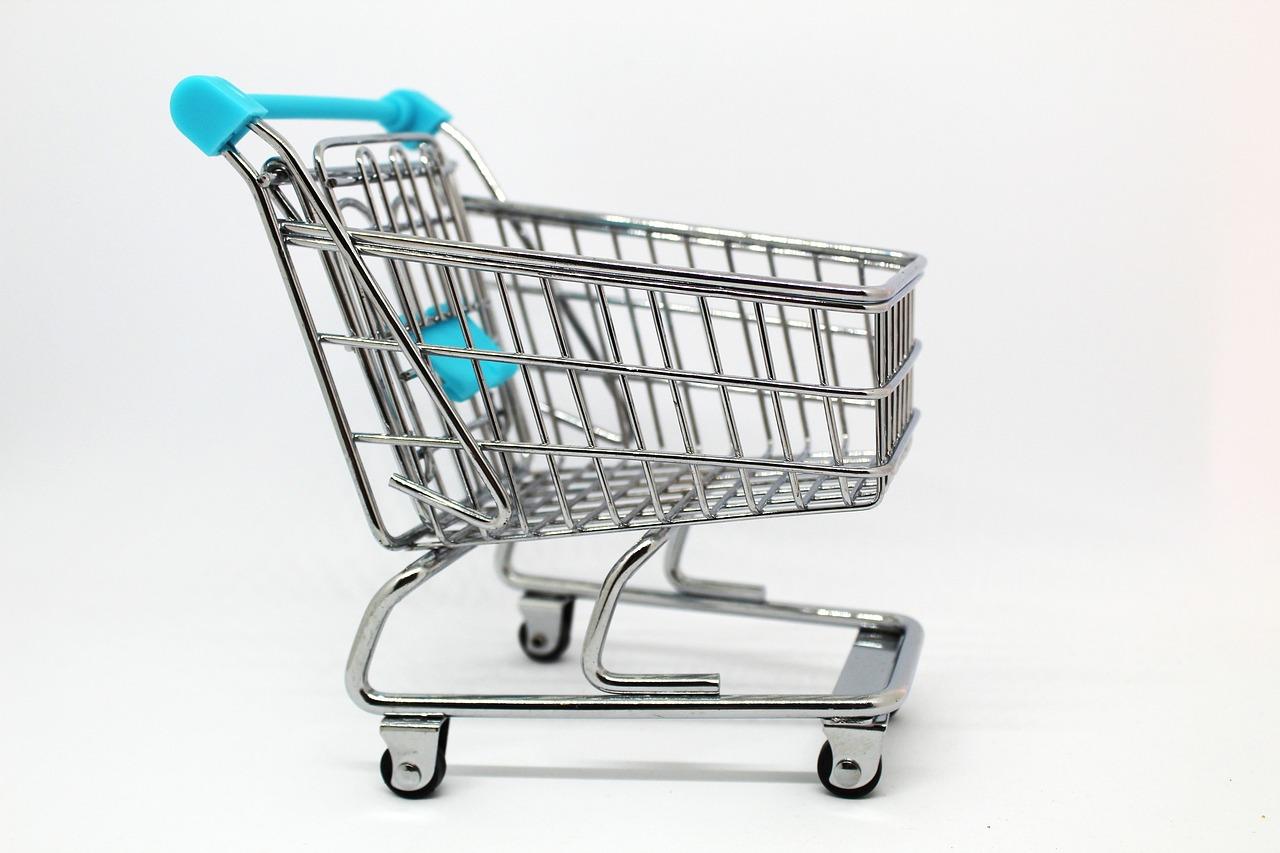 A tiny silver metal shopping cart on black wheels with light blue on the handlebar and child seat that has a white background.