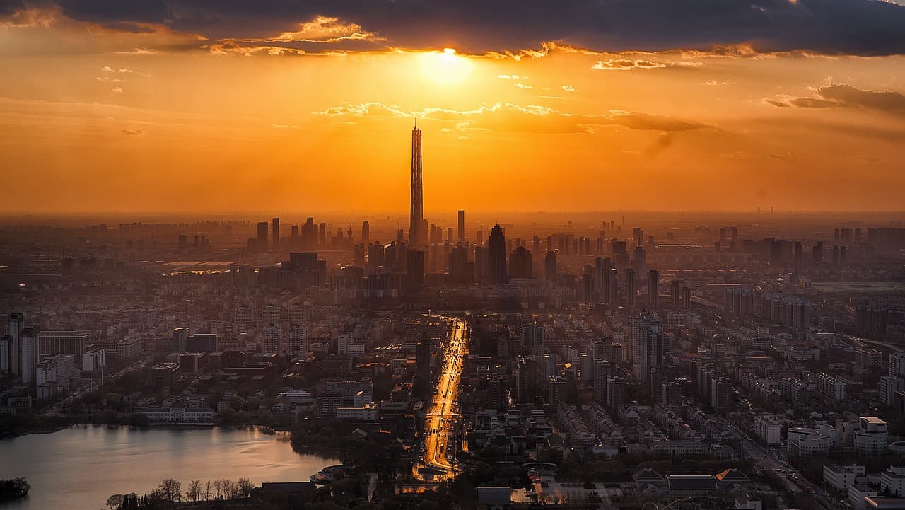 A city skyline that has a few skyscrapers in the middle of the city surrounded by large and small buildings during sunset.