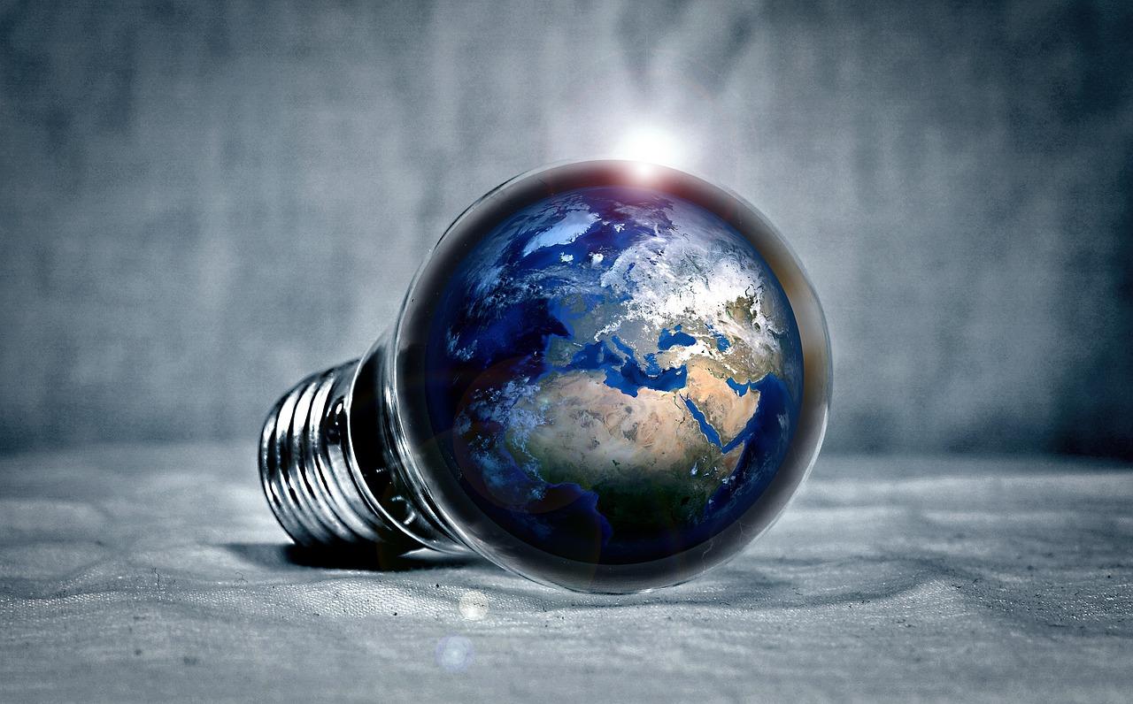 A lightbulb in a light gray room that has the planet Earth inside with blue oceans and green with white snow all around it.