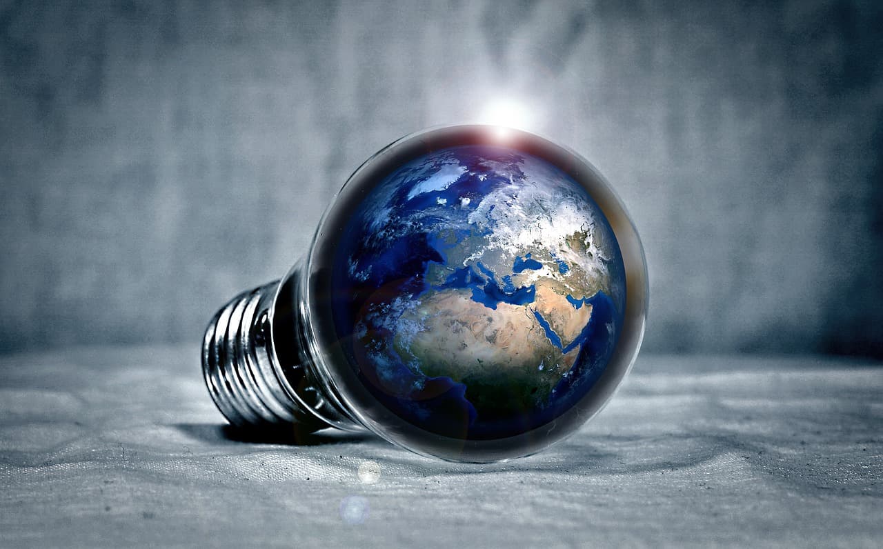 A lightbulb in a light gray room that has the planet Earth inside with blue oceans and green with white snow all around it.