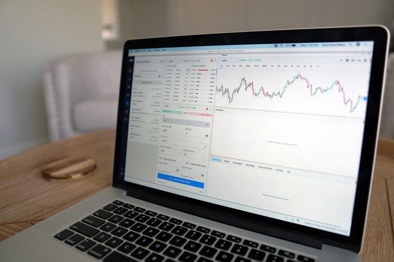 A gray Macbook with a white screen showing the crypto market on it going up and down in green and red with the order book.