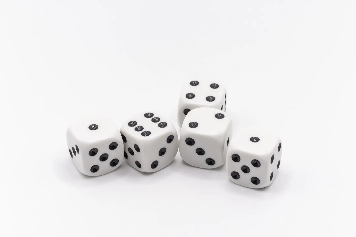 Five white dice sitting next to each other showing the numbers one, one, two, four, and six with black dots on a white table.
