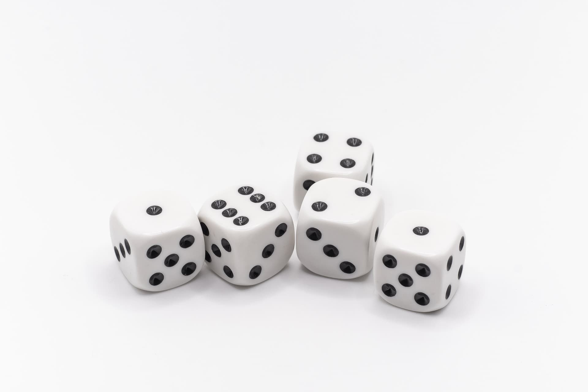 Five white dice sitting next to each other showing the numbers one, one, two, four, and six with black dots on a white table.