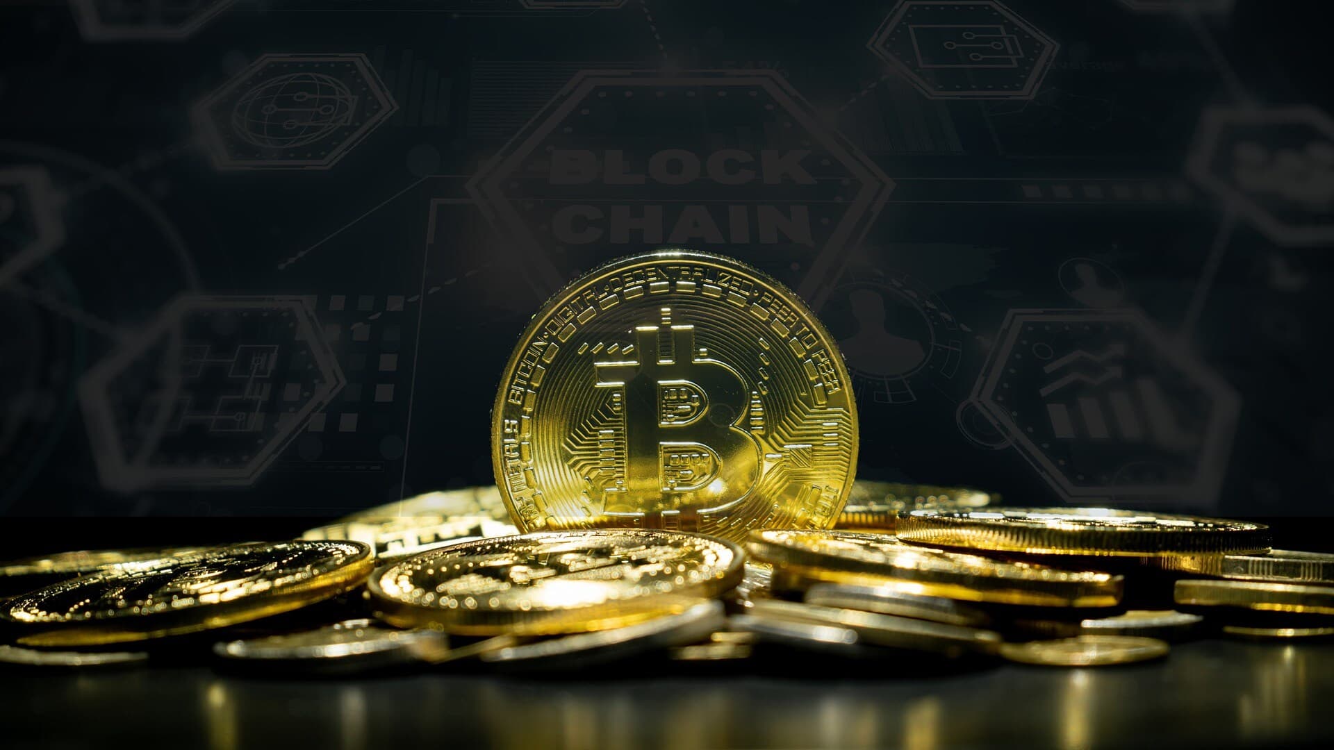 A golden Bitcoin crypto coin standing up in a pile of other coins with a dark colored background that says blockchain on it.