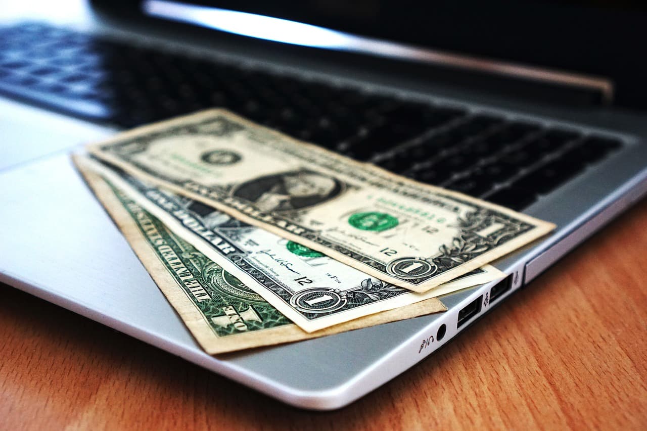 Three dollar bills sitting on top of a Macbook with two that are head side up and the other head side down on a wooden table.