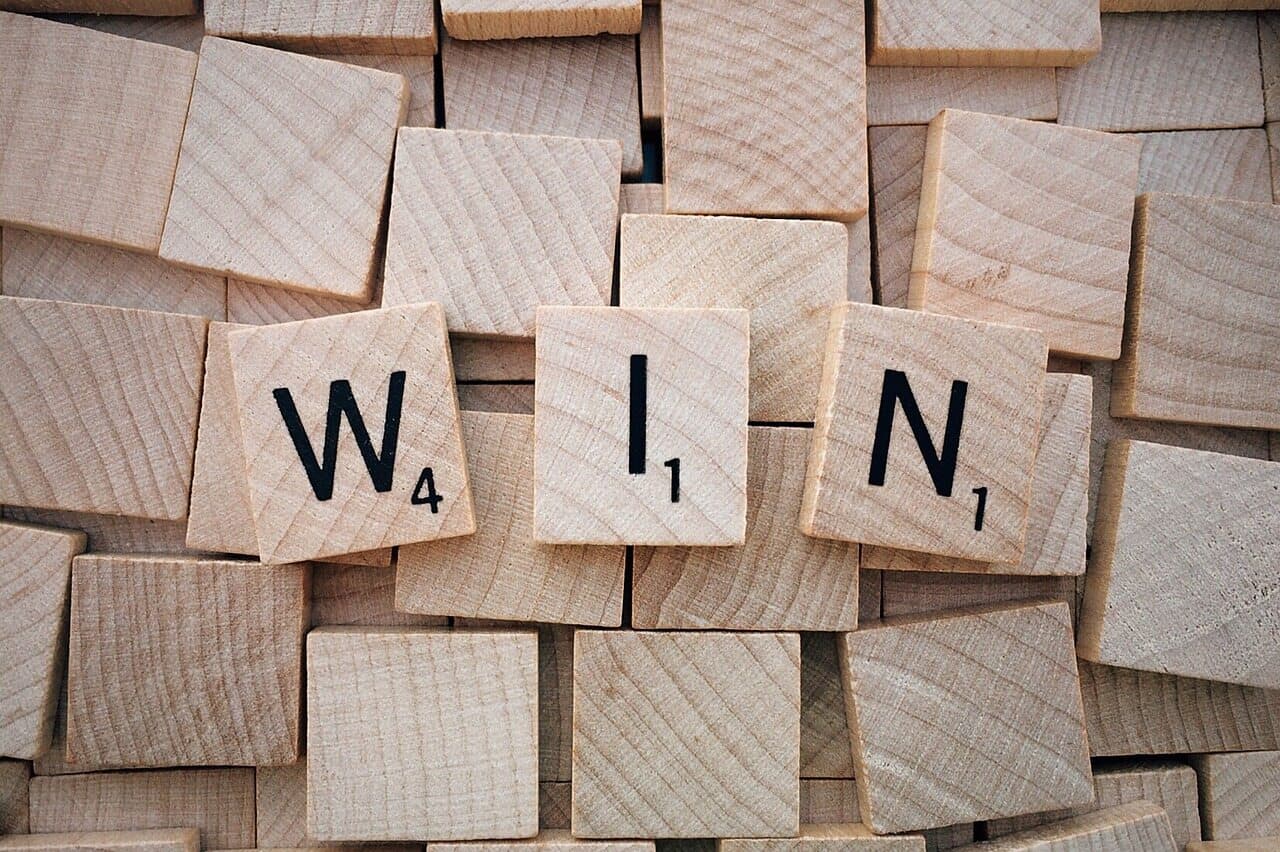 The word win spelled out with tiny wooden squares that have each letter written on them in black all on top of a pile of squares