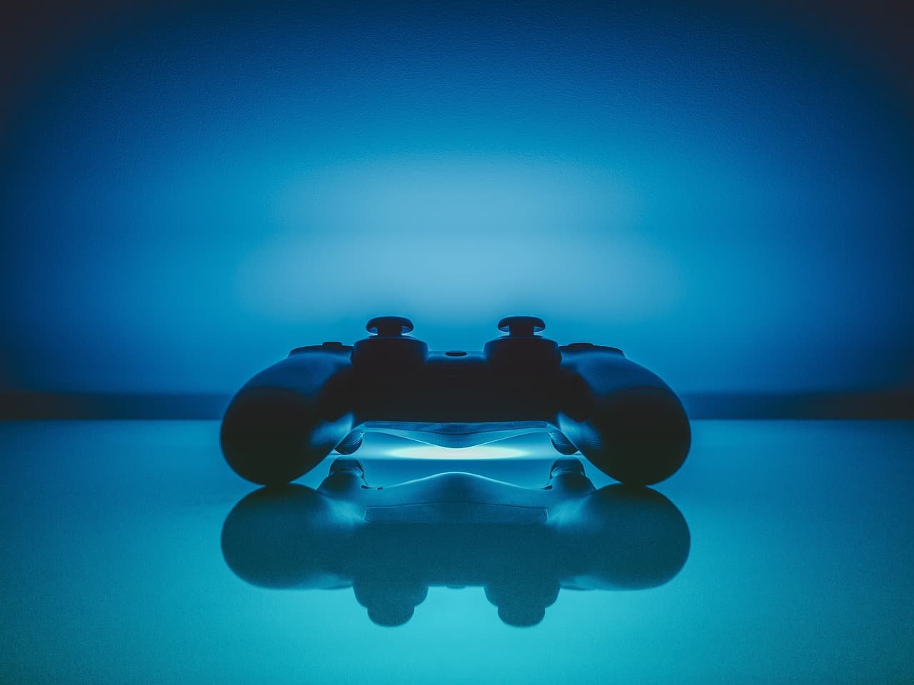 A gaming controller with a blue light on the top that is shining off of a reflective table and fully lighting up a dark room.