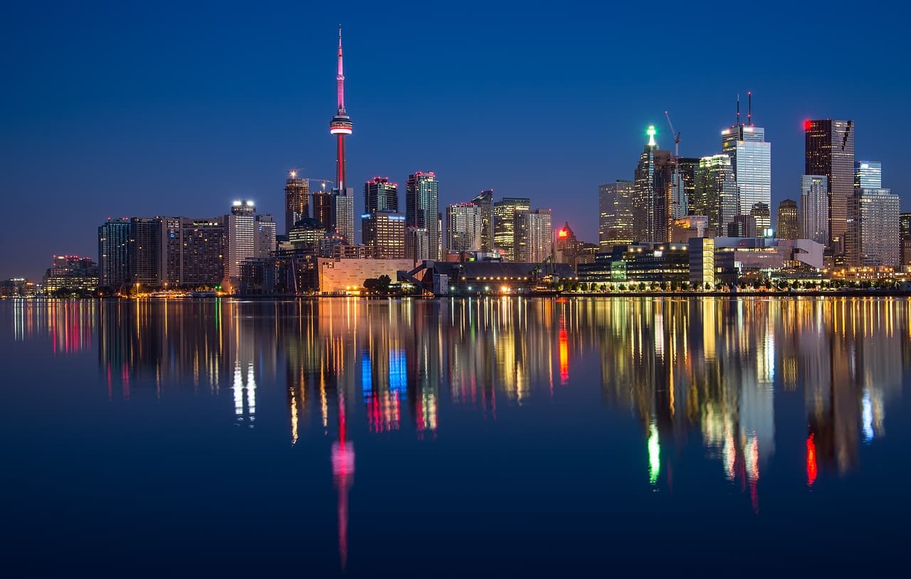 A water skyline that is covered in multiple large corporate buildings with water in front of them reflecting their bright image.