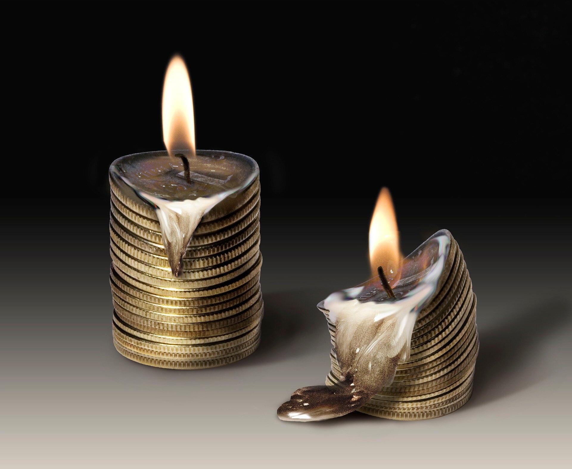 Two stacks of coins next to each other with candle wicks on top that are lit up and have been slowly melting the coin stacks.
