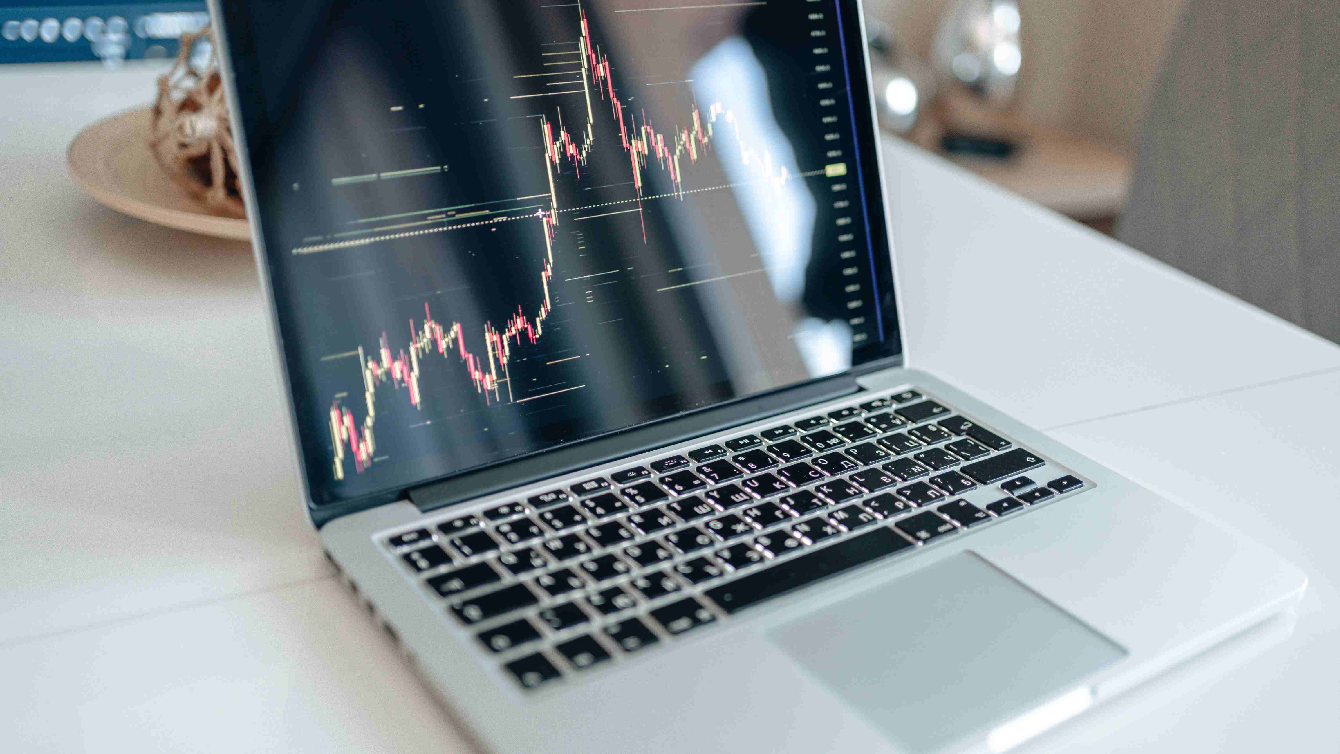 An Apple Macbook laptop showing the crypto market on it with a candle chart going up and down with green and red on a table.