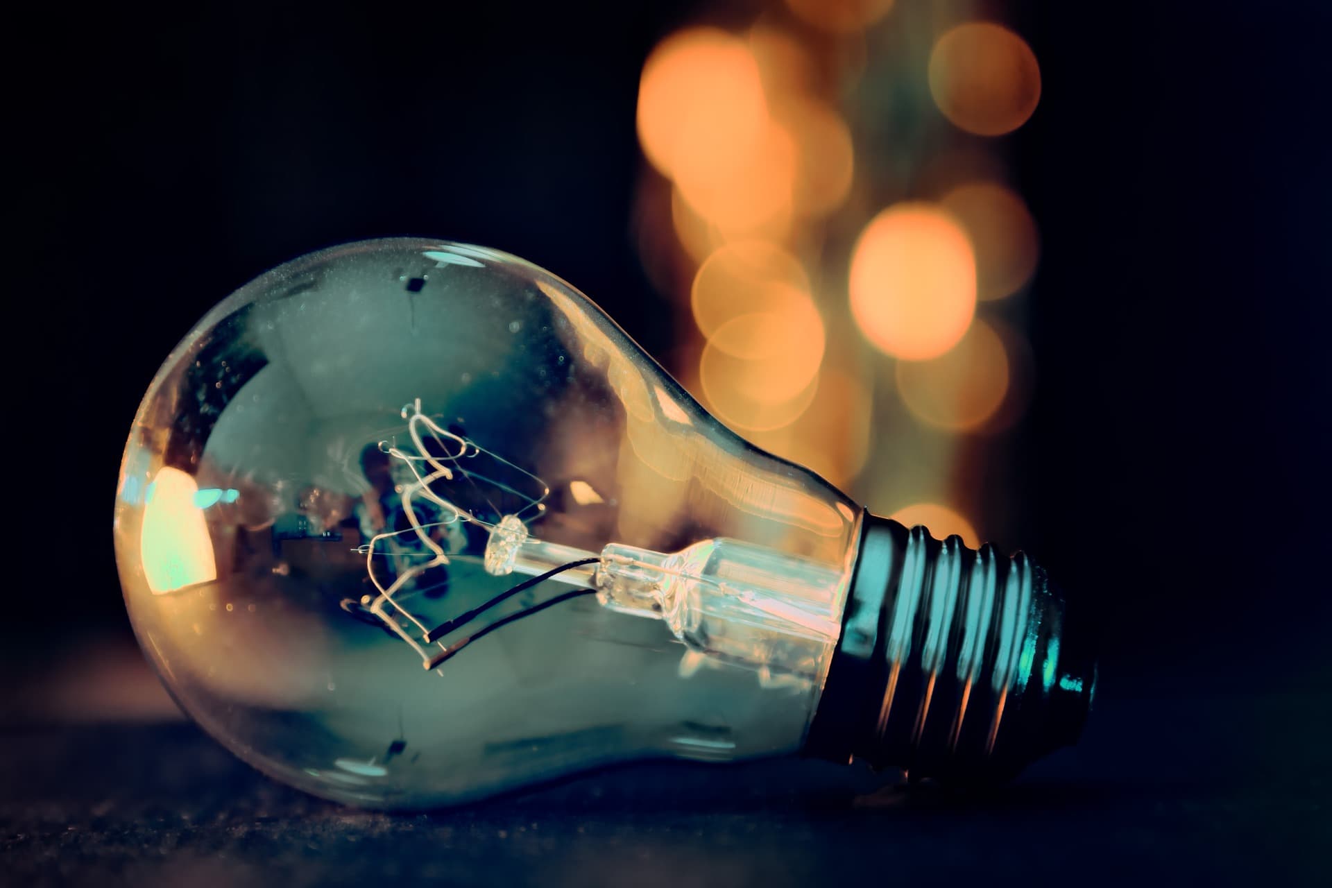 An unlit glass light bulb resting on its side in front of an unfocused set of lights that are in the shape of an upwards beam.