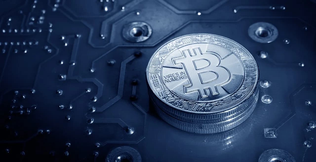 Four golden coins stacked on top of each other with the Bitcoin logo engraved in the top of them sitting on a large motherboard.