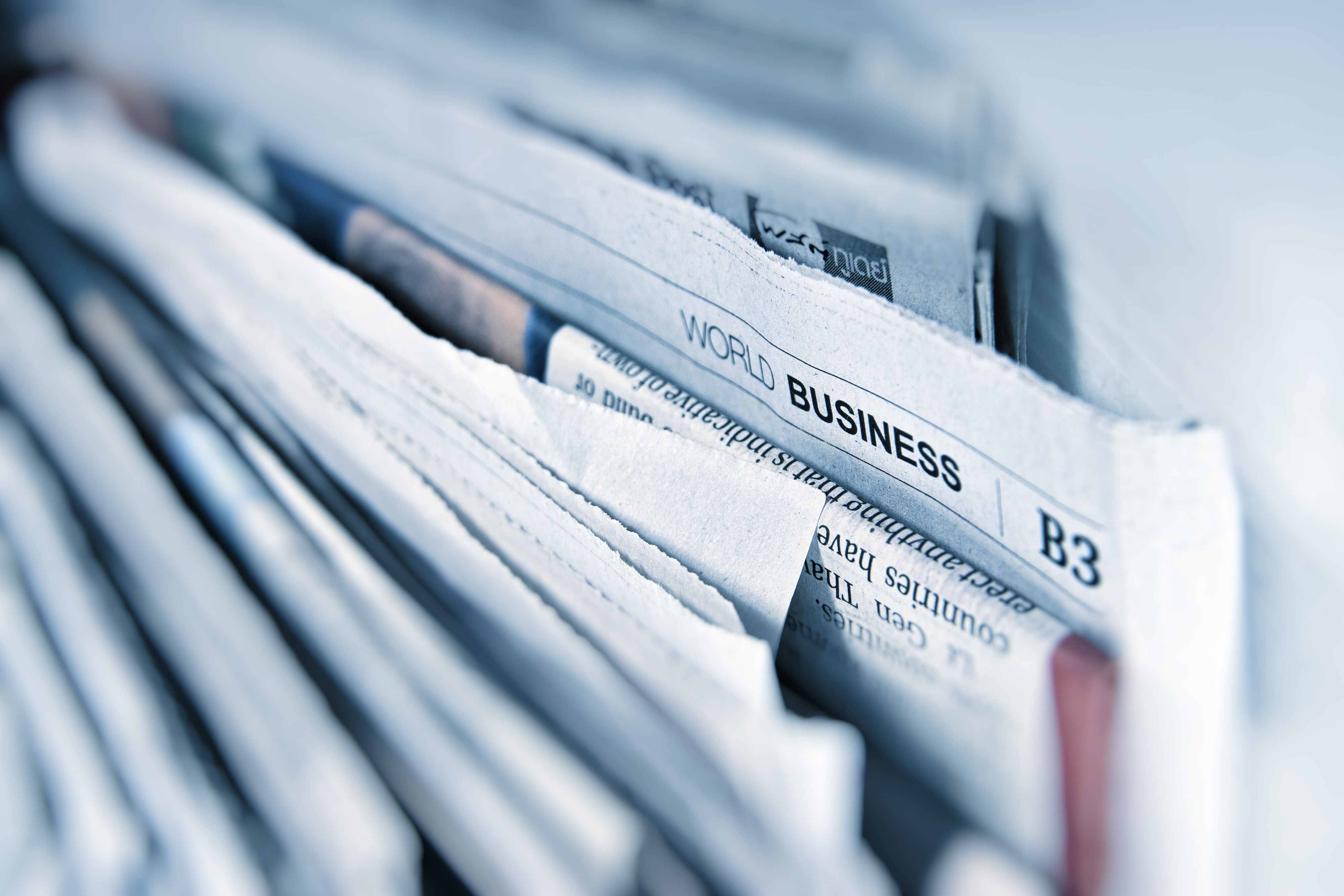 Multiple newspapers stacked on top of each other with the camera focused on one in the middle of them that says World Business.