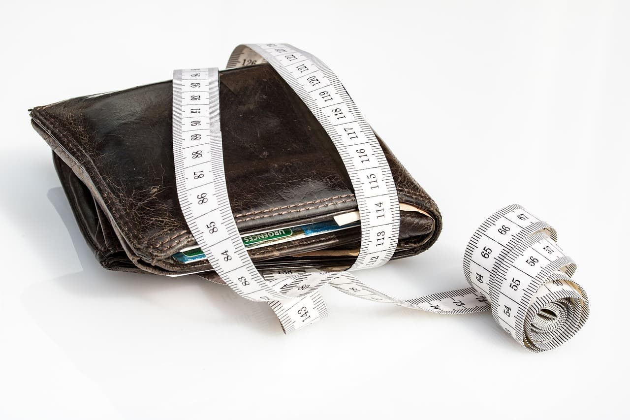 A darkly colored leather wallet with credit cards inside on its side resting on a white surface with a white tape measure.