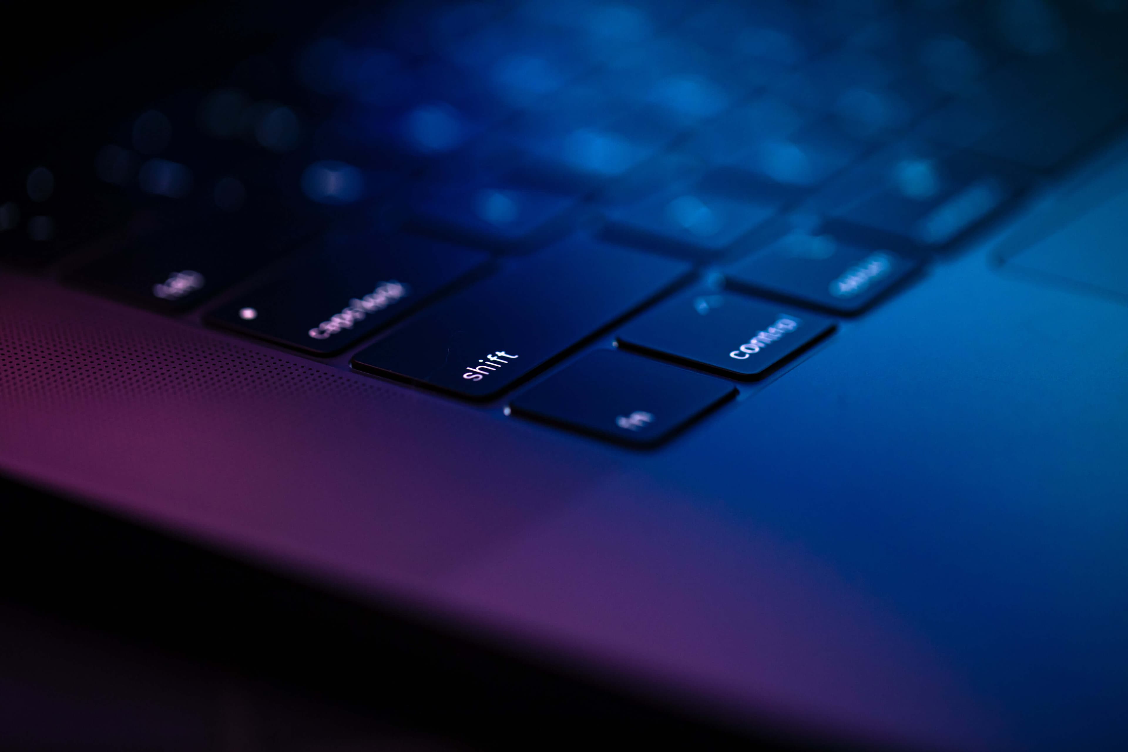 A small section of a Mac Laptop with a rainbow gradient light from red to blue and a black keyboard.