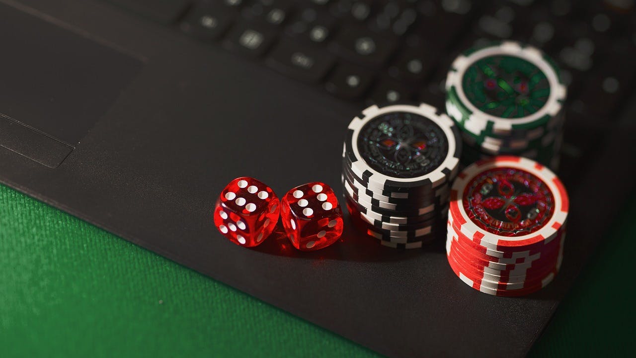 Two red dice that are see through showing sixes with white dots next to 3 stacks of poker chips all on top of a laptop keyboard.