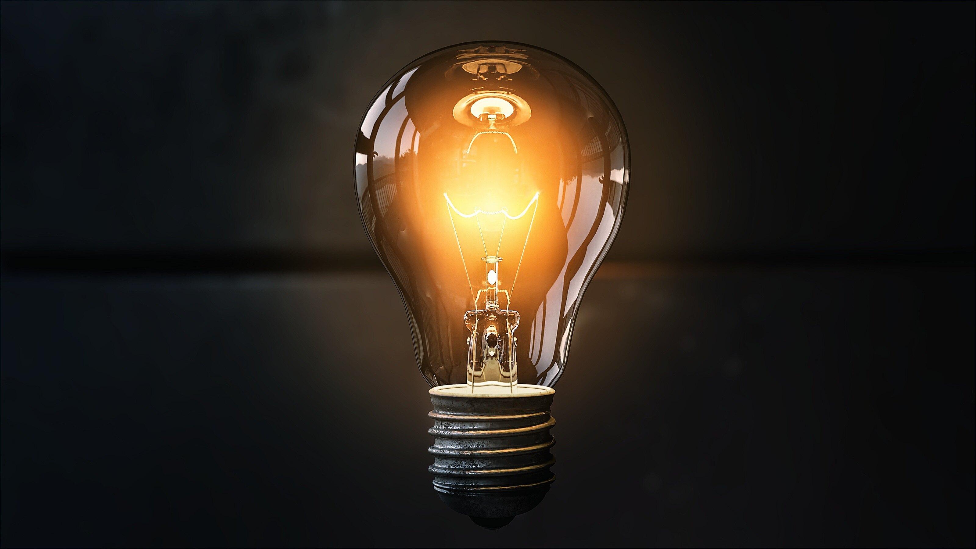 A shiny glass lightbulb that is dimly lit with an orange flow surrounding it that is vintage in front of a fully black background.
