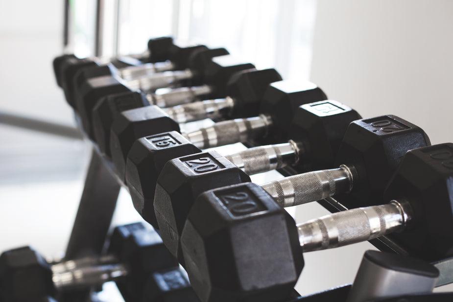 A rack of twenty metal dumbbells with black rubber covering the metal on each side of the shiny handles with weight numbers.