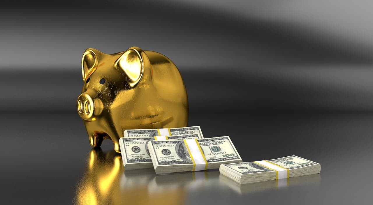 A golden piggy bank sitting on a table with three full stacks of one hundred dollar bills leaning on each other next to it.