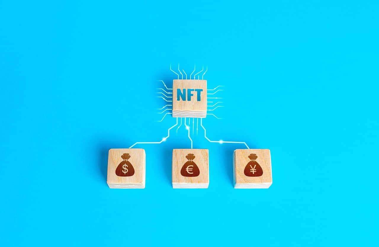 Four cubes of wood rest on a light blue surface with one labeled NFT and the other three displaying money bags in maroon.