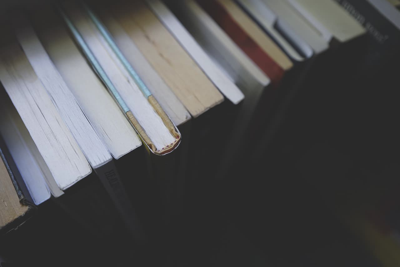 A row of multicolored books all in a line on a bookshelf all of which containing white pages with dark shadows behind them.