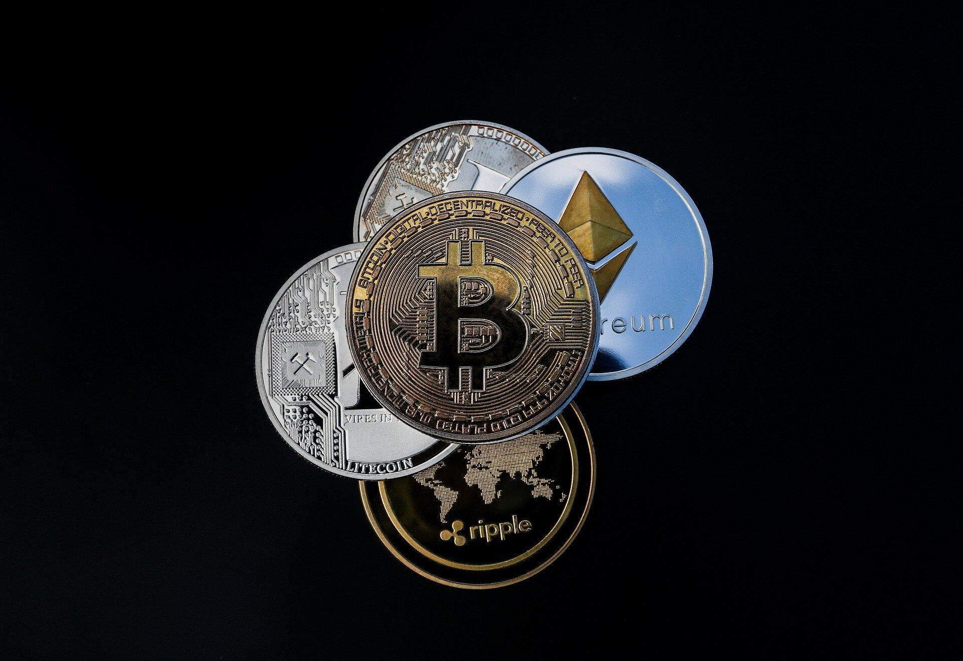 A golden bitcoin crypto coin sitting on top of a silver ethereum crypto coin and three other coins with a black background.