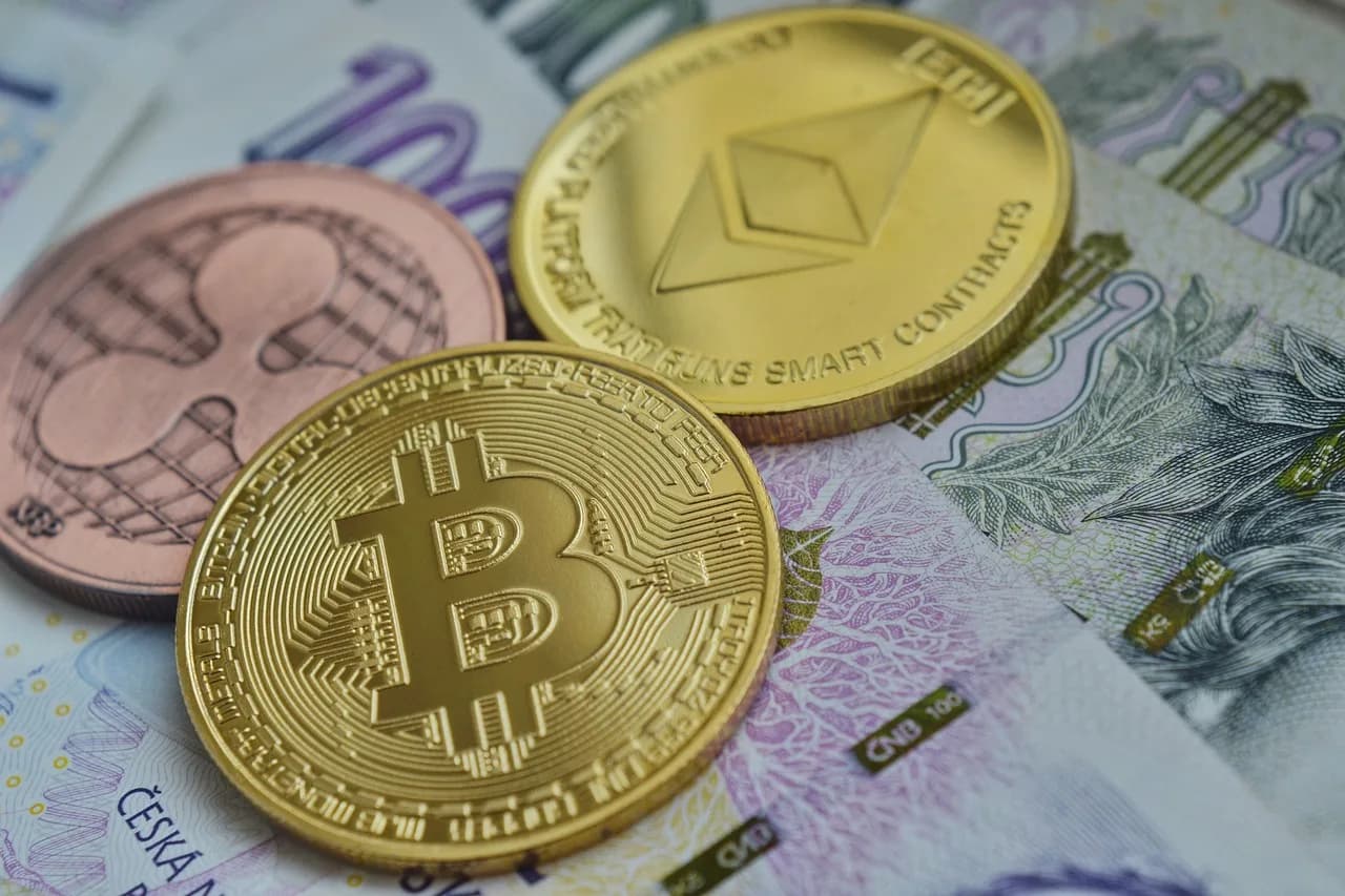 Golden Bitcoin, Ethereum, and Ripple golden crypto coins that are resting on top of each other all on top of a paper bill.