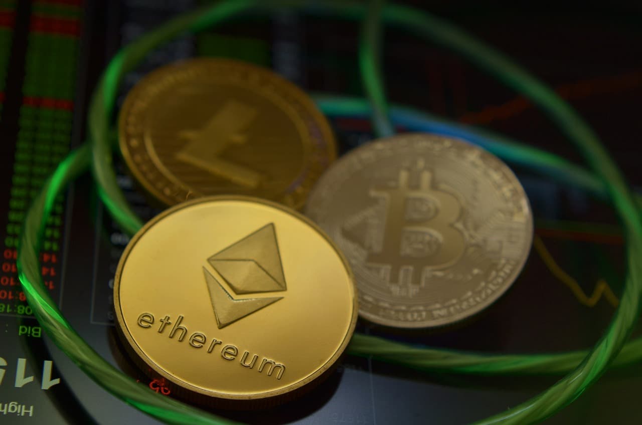 Three gold coins with the Bitcoin, Etheruem, and Litecoin logos on them with green wire and around them on computer parts.