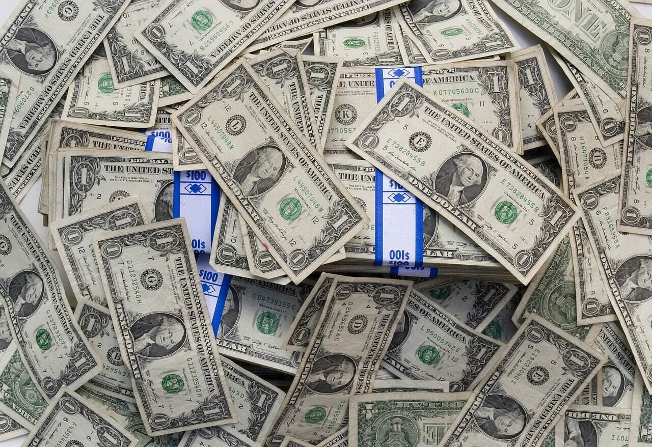 Multiple stacks of one dollar bills wrapped in blue currency straps sitting in a pile on top of more one dollar bills face up.