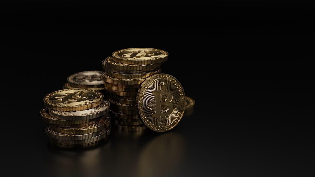 A bunch of golden coins in three different stacks all with the Bitcoin logo on them and one coin in front with the logo on it.