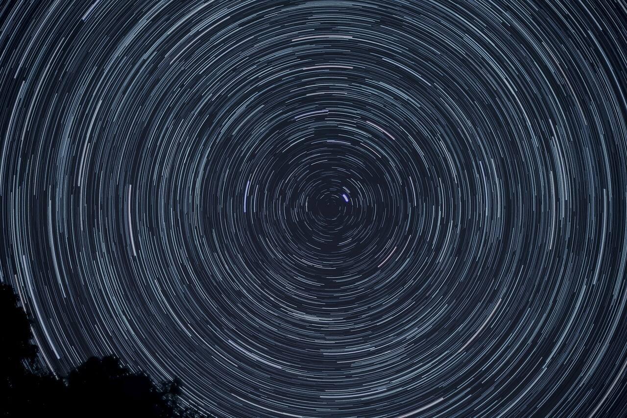 A bunch of stars in the sky spinning in circles to make multiple different rings of stars under the blue space filled sky.