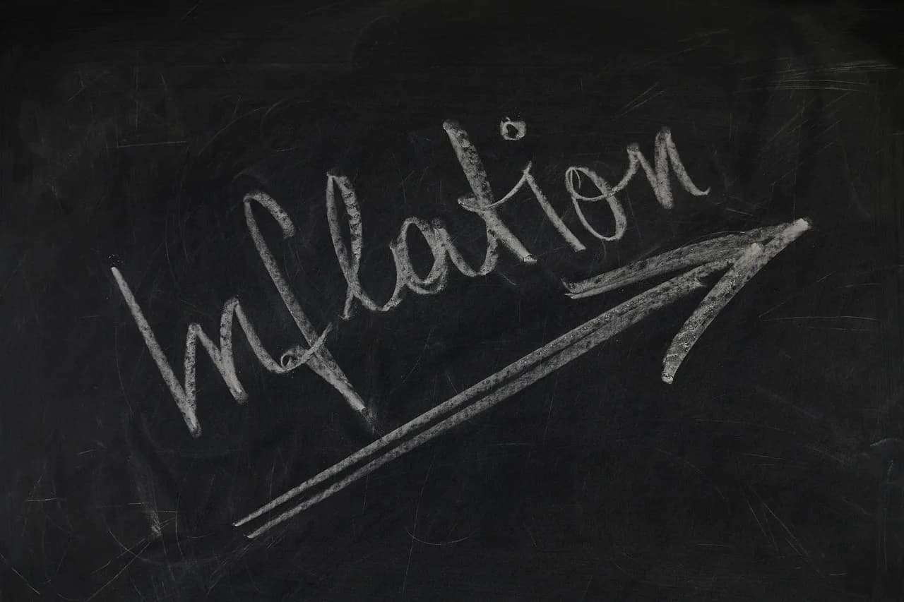 A black board with a bunch of white scratches on it from previous writing that has the word inflation written on it in chalk.