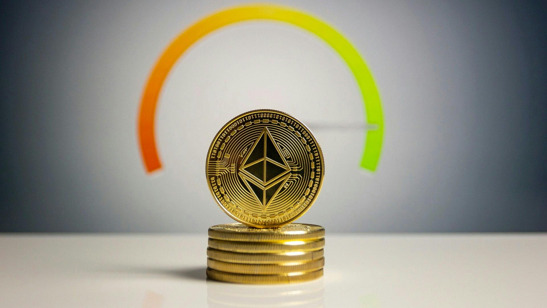 A golden Ethereum crypto coin sitting on its side on top of a stack of other golden coins in front of a gauge pointing green.
