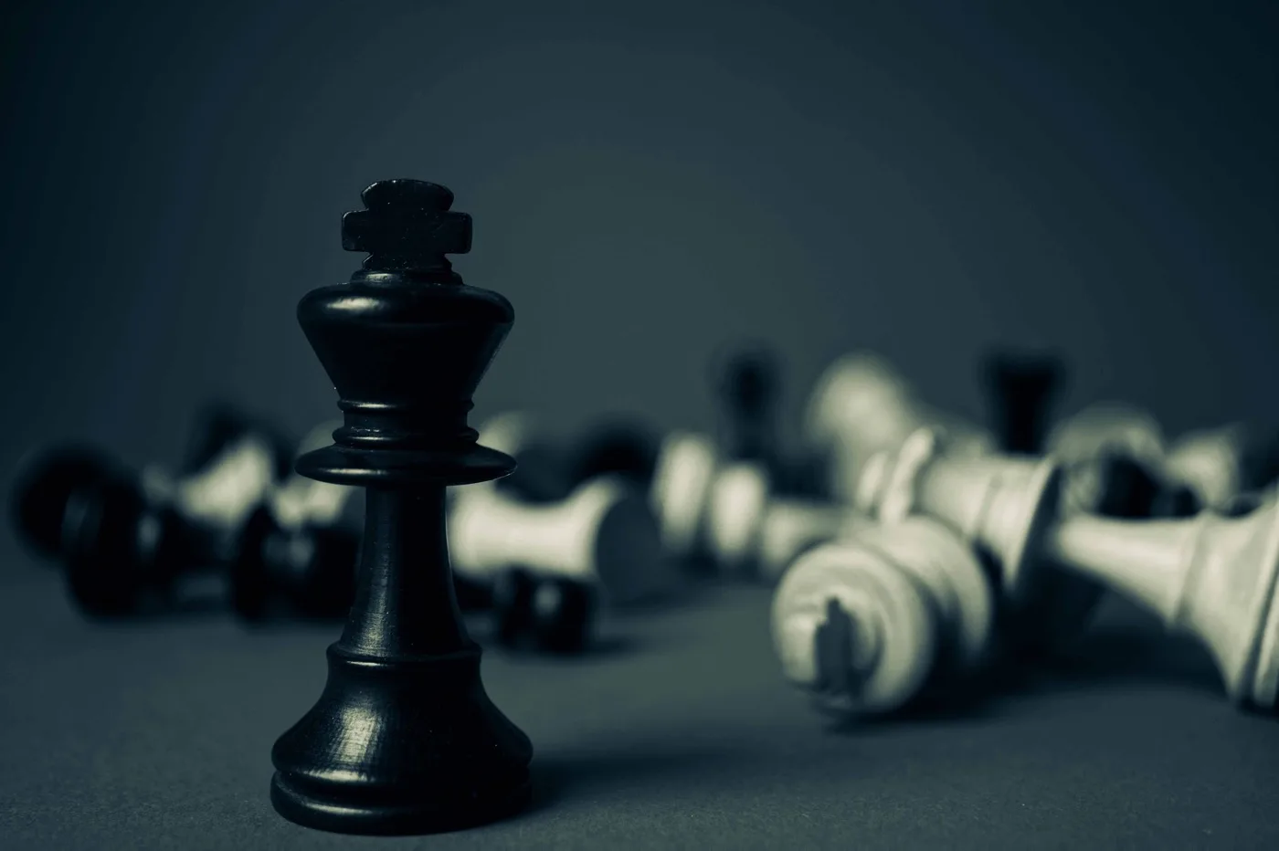 A bunch of chess pieces all in a dark gray box while all being knocked down to the ground other than the black side’s king.
