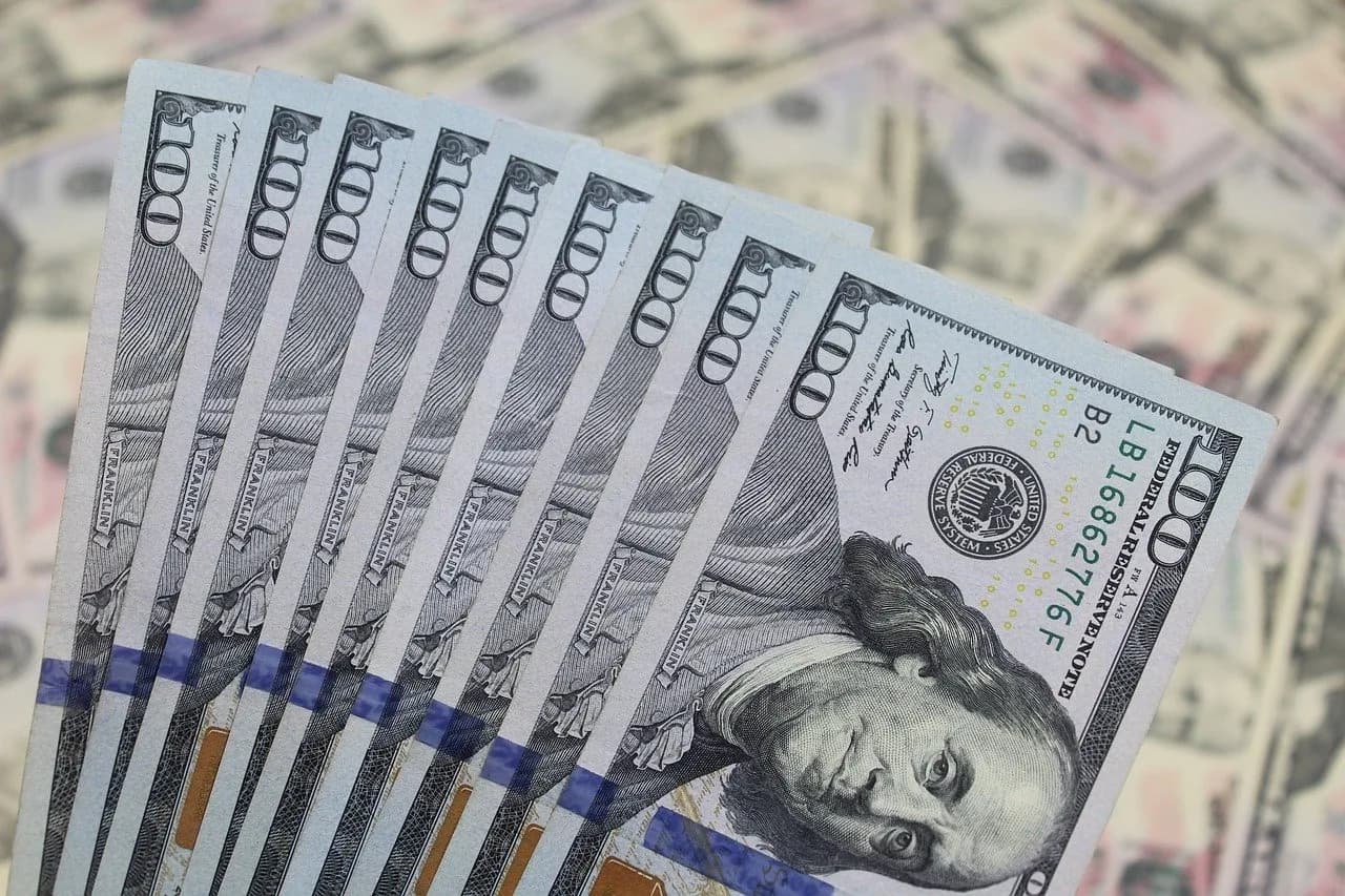 Nine on hundred dollar bills all stacked together and spread out like a fan with the faces upwards in front more bills behind.