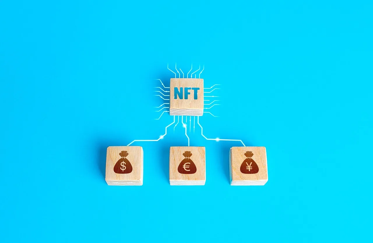 Four cubes of wood rest on a light blue surface with one labeled NFT and the other three displaying money bags in maroon.